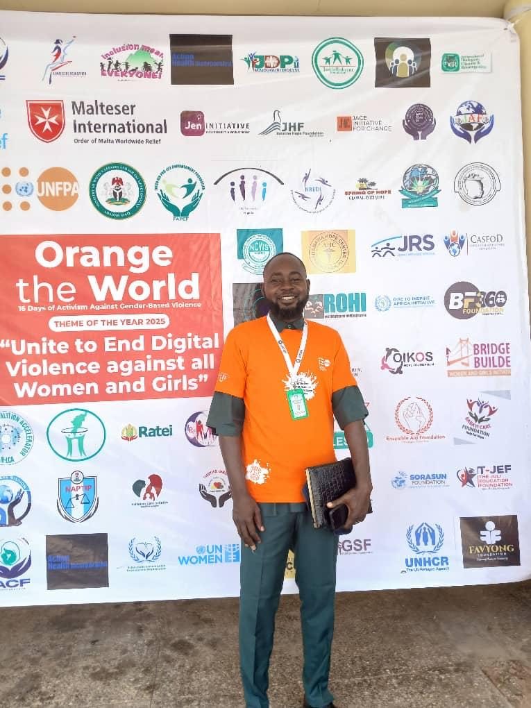 A man in an orange campaign T-shirt standing in front of a wall of partner logos including JHF.