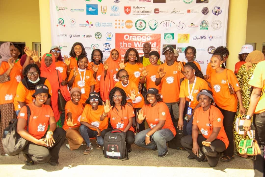 JHF staff and partner organisations in orange T-shirts raising their hands in front of an Orange the World banner.